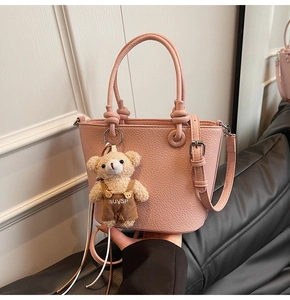 Borsa a secchiello rosa con trama litchi su divano grigio e ciondolo a orso