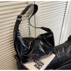 Detail of glossy black hobo bag featuring wide shoulder strap and silver metal buckle