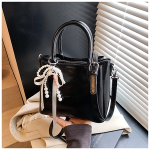 Close-up of black bucket bag featuring glossy finish and a pearl bow charm detail