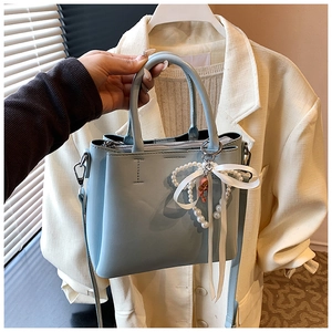 Close-up of a light blue PU leather bucket bag with pearl bow charm and stitching detail