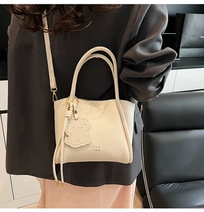 Detailed side view of a beige lychee pattern bucket bag with a dog charm and shoulder strap