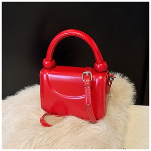 Detail view of mini red glossy handbag with circular top handle and silver buckle