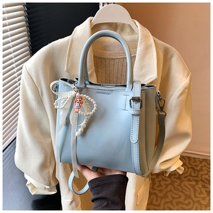 Detail of light blue bucket bag with pearl charm and white ribbon on neutral background