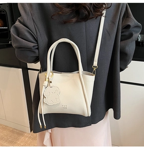 Close-up of off-white lychee leather tote bag with Pan Tor logo and cute charm