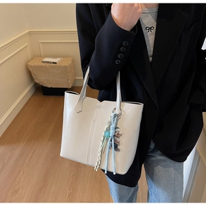 Close-up of cream-colored glossy tote bag with cartoon dog charm and stitched details