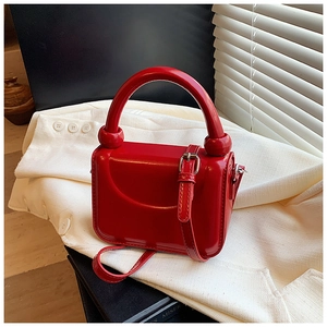 Detail of vibrant red glossy leather handbag with top handle and metal buckle strap