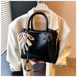 Detail of black leather bucket bag with white pearl charm and bow accessory for women