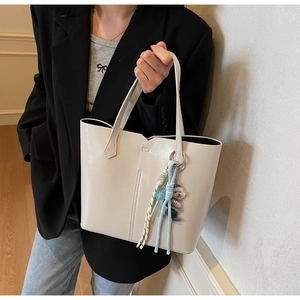 Detail of a white faux leather tote bag with wavy edges and decorative charm