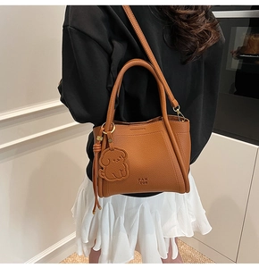 Detail of reddish-brown lychee grain bucket bag featuring a cute dog charm and logo
