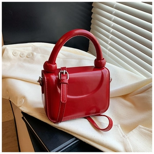 Detail of red mini crossbody bag with silver buckle and round handle on white suit