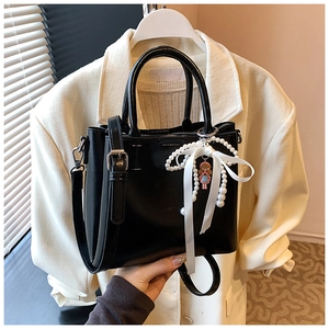 Detail of black faux leather bucket bag with pearl bow charm on a white blazer background
