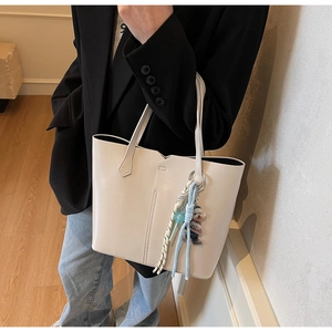 Close-up of cream tote bag featuring vertical stitching and a cute dog charm accessory