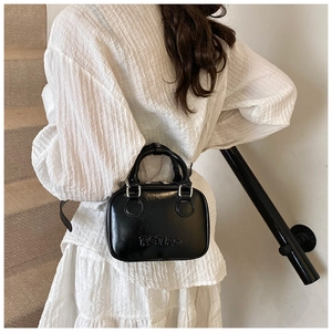 Close-up of black glossy leather retro handbag with embossed letters and silver hardware