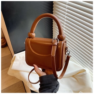 Detail of brown mini square bag with sleek handle and spherical metal base studs