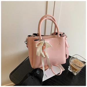 Detail of pink bucket bag featuring a pearl bow charm and dolls on a black texture table