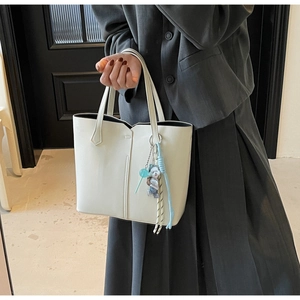 Close-up of white tote bag with wave-edge design and fashion pendants on shoulder