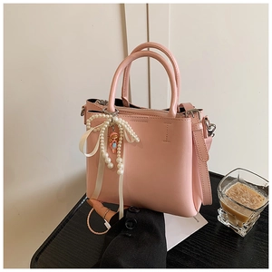 Detail of pink bucket bag with pearl pendant, ribbon bow, and latte on wooden surface