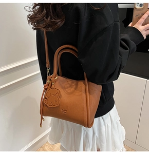 Close-up of caramel brown pebble leather bucket bag with dog charm and PAN TOR logo