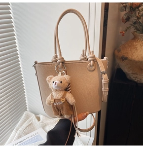 Dettaglio borsa a secchiello in pelle beige con ciondolo a orsetto e tracolla sottile