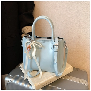 Detail of light blue bucket bag with pearl bow and doll charm on a vintage book