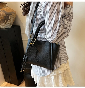 Detail of black lychee grain leather handbag with gold hardware and bear charm