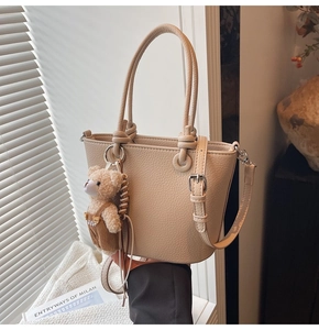 Dettaglio borsa beige con grana litchi, tracolla e ciondolo a forma di orso