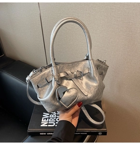 Detalle de bolso de hombro plateado con textura plisada y un colgante de corazón metálico