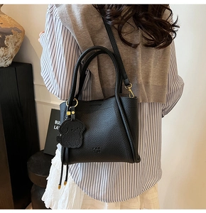 Detail of black lychee grain leather bucket bag with dog pendant and gold hardware