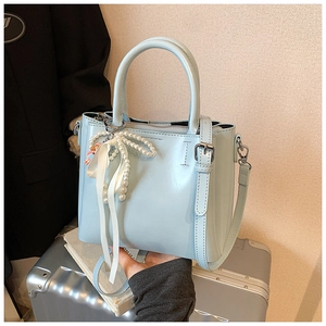 Light blue bucket bag with pearl bow charm and silver hardware on a silver suitcase