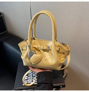 Detalle del bolso tipo cubo amarillo con hebilla decorativa y un colgante de corazón