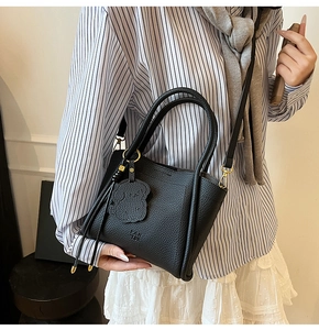 Detail of black lychee grain leather crossbody bag with cute bear charm and gold hardware