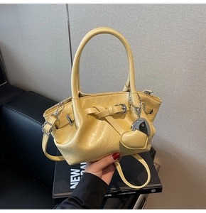 Detalle de bolso tipo saco plisado amarillo con colgante de corazón y correa de plata