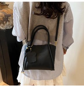Detail of black litchi grain bucket bag featuring a hand strap and cute animal charm