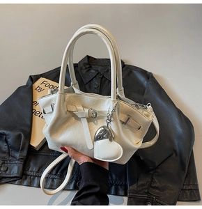 Detalle de bolso tipo cubo crema con textura de cuero plisado y colgante de corazón