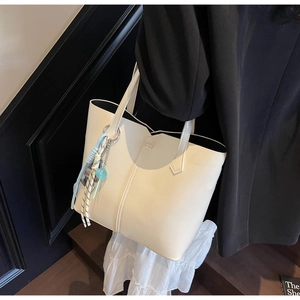 Detail of a cream minimalist tote bag with decorative tassel worn over a black blazer