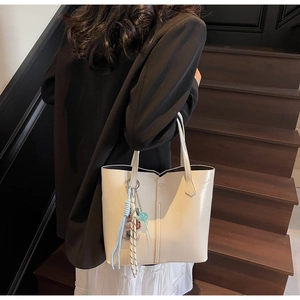 Detail of cream white faux leather tote bag with V-shaped cut and woven pendant charm