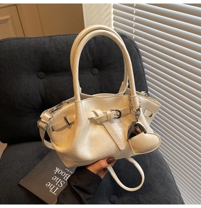 Detalle del bolso tipo cubo crema con diseño plisado y colgante de corazón en silla gris