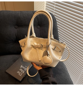 Detalle del bolso de cuero crema con herrajes plateados y un colgante en forma de corazón