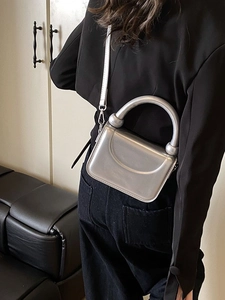 Sleek silver metallic handbag with curved lines and detachable strap on model back