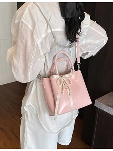 Pink bucket bag with bow and pearl chain decoration shown from a stylish side view