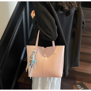 Detail of soft pink tote bag featuring slim straps and a woven pendant on a staircase