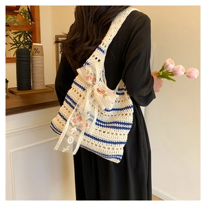 Détail du sac tricoté à rayures bleues et nœud en dentelle florale sur robe noire