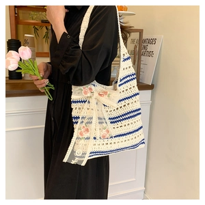 Détail d'un sac cabas en paille tissé avec rayures bleues et nœud en dentelle fleurie