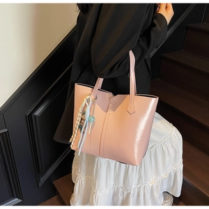 Pink tote bag detail with tassel charm worn by model on dark staircase background