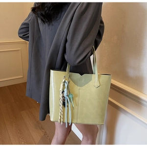 Detail of light green faux leather tote bag featuring a geometric cutout and woven charm