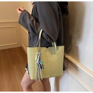 Detail of light green tote bag featuring geometric cuts and a woven decorative charm