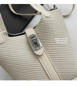 Detail of metal twist-lock buckle on cream woven straw bucket bag with leather trim