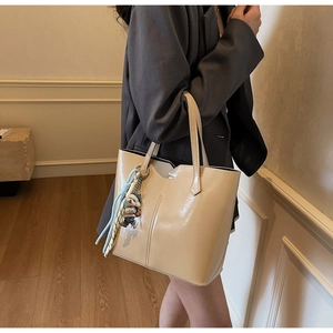 Detail of cream tote bag with glossy finish and cute bear charm hanging on handle