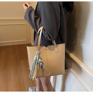Detail of a beige leather tote bag featuring stylish vertical stitching and a cute bear charm