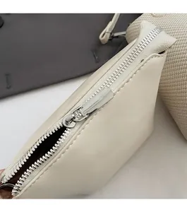 Close-up of smooth silver metal zipper on cream white leather handbag with matte finish